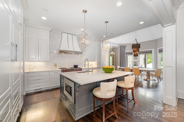 15603 June Washam Rd, Davidson, NC 28036 - kitchen with custom range hood, stainless steel microwave, decorative backsplash, a kitchen island with sink, and white cabinetry