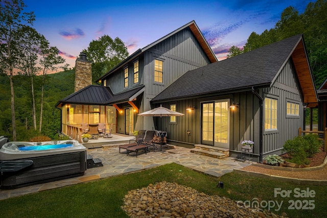1416 E Clubhouse Rd Unit 73, Sylva, NC 28779 - back of property at dusk with board and batten siding, a hot tub, a patio, roof with shingles, and a chimney
