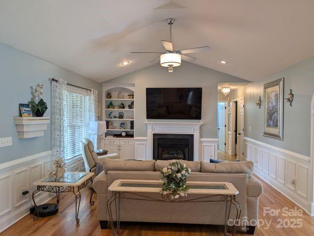 1764 Pipers Ridge Cir NW, Conover, NC 28613 - living area featuring a decorative wall, a ceiling fan, a wainscoted wall, a glass covered fireplace, and wood finished floors