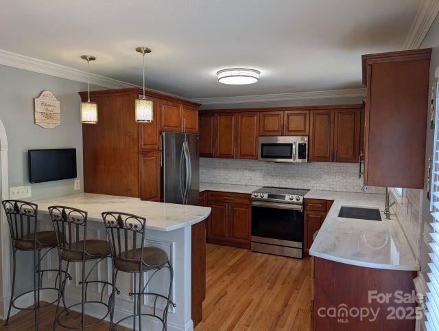 1764 Pipers Ridge Cir NW, Conover, NC 28613 - kitchen with stainless steel appliances, a breakfast bar, tasteful backsplash, a peninsula, and light wood-style flooring