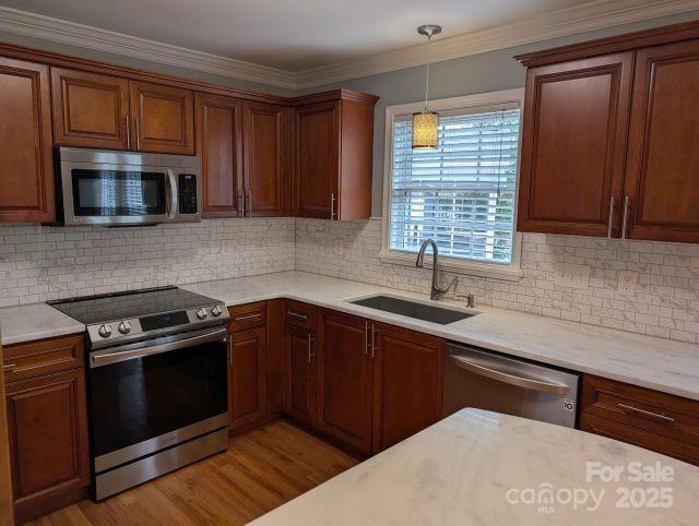 1764 Pipers Ridge Cir NW, Conover, NC 28613 - kitchen with appliances with stainless steel finishes, light wood-style flooring, decorative light fixtures, tasteful backsplash, and ornamental molding