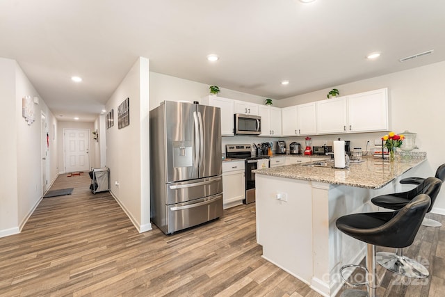 418 Winsley Dr, Salisbury, NC 28147 - kitchen with stainless steel appliances, a peninsula, light wood-style flooring, a kitchen bar, and white cabinetry