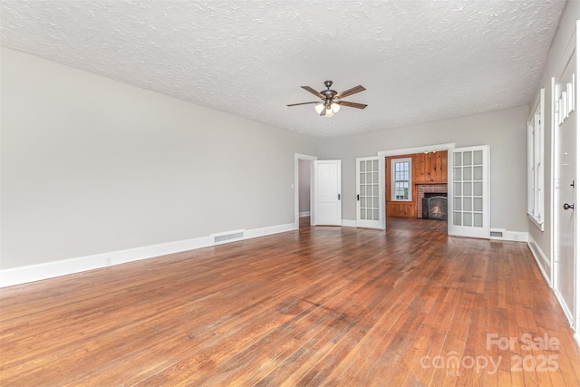 309 E Main St, Lattimore, NC 28089 - unfurnished living room with wood-type flooring, ceiling fan, a textured ceiling, a brick fireplace, and french doors