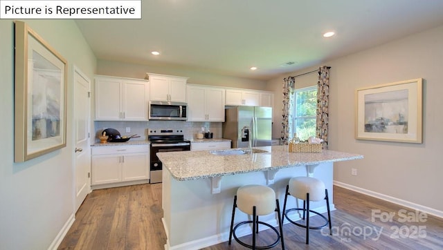 1400 Secrest Commons Dr, Monroe, NC 28112 - kitchen with appliances with stainless steel finishes, wood finished floors, white cabinets, a breakfast bar area, and tasteful backsplash