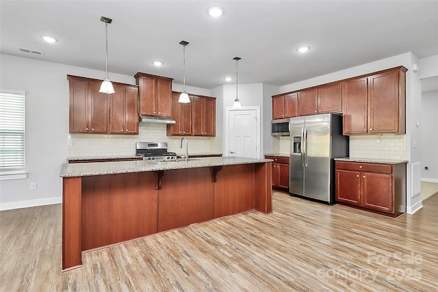 7079 Waterwheel St SW, Concord, NC 28025 - kitchen featuring stainless steel appliances, under cabinet range hood, light wood-style flooring, tasteful backsplash, and a center island with sink