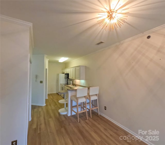 1410 4th Street Dr NW Unit 303, Hickory, NC 28601 - kitchen featuring crown molding, wood finished floors, a kitchen breakfast bar, black microwave, and white cabinetry