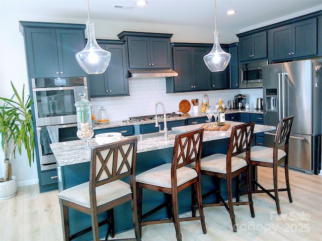 1141 Overlake Dr, Belmont, NC 28012 - kitchen with appliances with stainless steel finishes, decorative backsplash, light wood-style flooring, light stone counters, and a kitchen bar