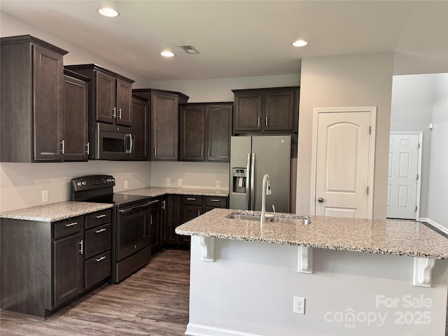 11109 Pond Valley Ct, Charlotte, NC 28269 - kitchen featuring appliances with stainless steel finishes, dark brown cabinets, dark wood-type flooring, a breakfast bar area, and light stone countertops