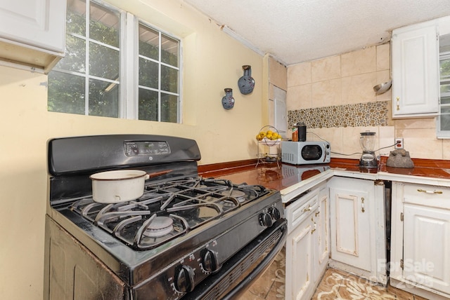 8301 Pine Oak Rd, Waxhaw, NC 28173 - kitchen with black range with gas stovetop, white microwave, tasteful backsplash, white cabinets, and a textured ceiling