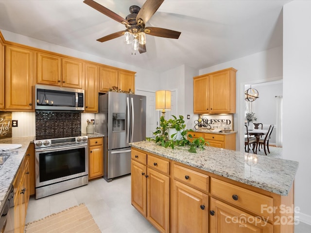 11126 Windgate Ct, Tega Cay, SC 29708 - kitchen featuring appliances with stainless steel finishes, a ceiling fan, backsplash, light stone countertops, and a center island