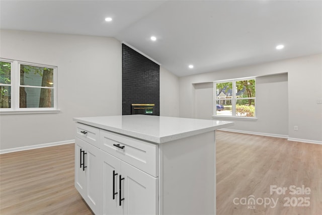 5534 Great Wagon Rd, Charlotte, NC 28215 - kitchen with light wood-style floors, vaulted ceiling, a brick fireplace, light countertops, and white cabinetry