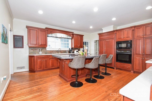 711 Yadkin St, Albemarle, NC 28001 - kitchen with black appliances, light wood finished floors, a kitchen breakfast bar, a kitchen island, and ornamental molding
