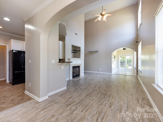 621 Pine Links Dr, Tega Cay, SC 29708 - unfurnished living room with a ceiling fan, arched walkways, light wood-style flooring, ornamental molding, and a glass covered fireplace