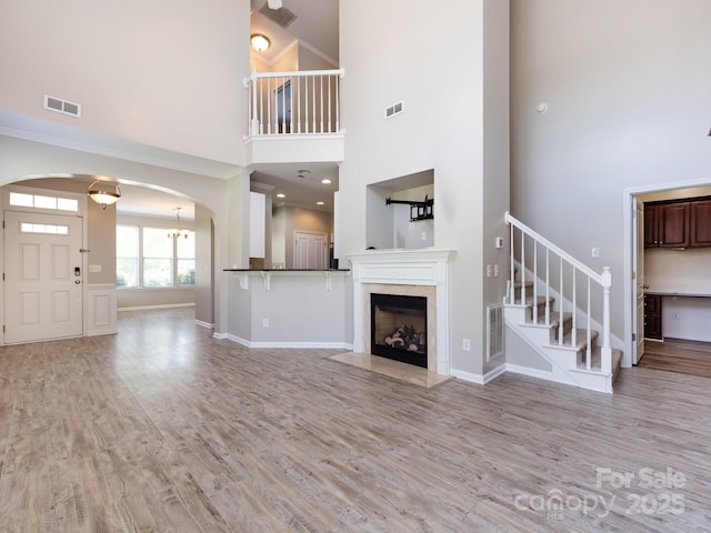 621 Pine Links Dr, Tega Cay, SC 29708 - unfurnished living room featuring stairs, arched walkways, a towering ceiling, light wood-type flooring, and a fireplace