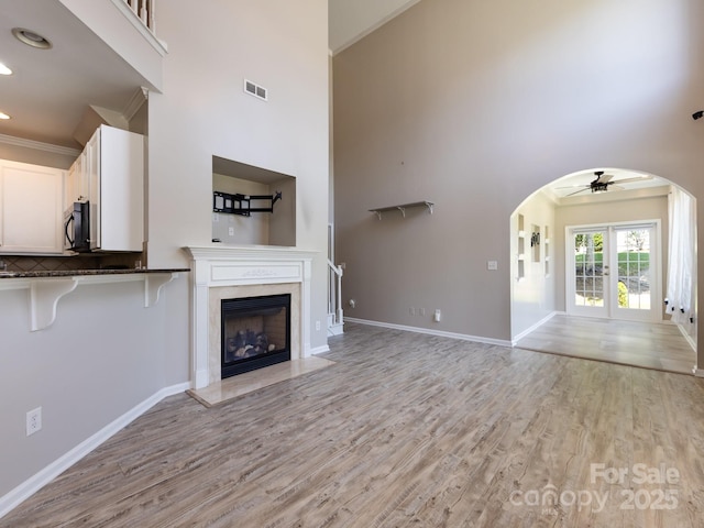 621 Pine Links Dr, Tega Cay, SC 29708 - unfurnished living room with arched walkways, a ceiling fan, light wood-type flooring, a towering ceiling, and a premium fireplace