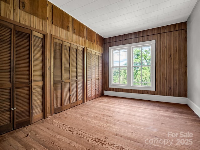 1111 Bills Creek Rd, Lake Lure, NC 28746 - unfurnished bedroom with wood walls, light wood-style flooring, and two closets