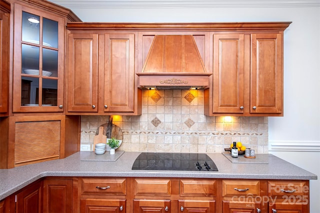 7554 Bluestar Ln, Charlotte, NC 28226 - kitchen with custom range hood, black electric stovetop, tasteful backsplash, glass insert cabinets, and brown cabinetry