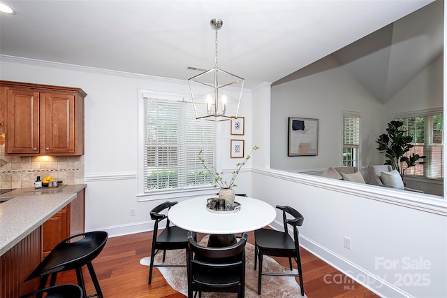 7554 Bluestar Ln, Charlotte, NC 28226 - dining space featuring a chandelier, dark wood-style floors, vaulted ceiling, and crown molding