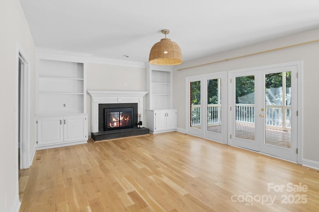 1134 Willow Oaks Trl, Matthews, NC 28104 - unfurnished living room featuring light wood-style flooring, french doors, a glass covered fireplace, built in shelves, and crown molding
