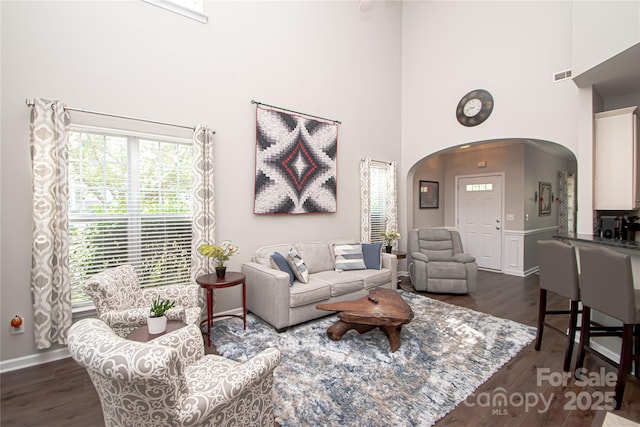 1304 Hammond Dr, Matthews, NC 28104 - living room featuring arched walkways, a towering ceiling, dark wood-type flooring, and a wainscoted wall