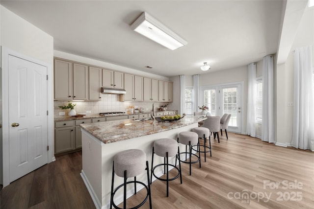 14801 Provence Ln, Charlotte, NC 28277 - kitchen with under cabinet range hood, stainless steel gas stovetop, a kitchen breakfast bar, light wood finished floors, and decorative backsplash