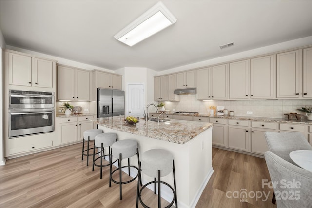 14801 Provence Ln, Charlotte, NC 28277 - kitchen with appliances with stainless steel finishes, under cabinet range hood, a breakfast bar, light wood finished floors, and decorative backsplash