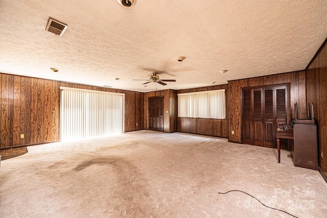 3954 E Burke Blvd, Connelly Springs, NC 28612 - unfurnished living room featuring a textured ceiling, wood walls, ceiling fan, carpet, and plenty of natural light