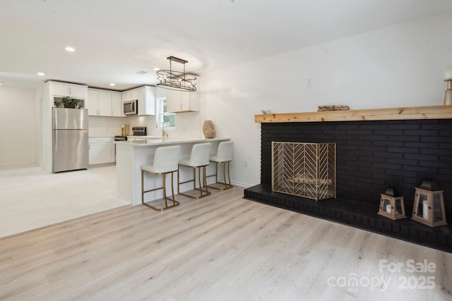 5420 Gwynne Ave, Charlotte, NC 28205 - kitchen featuring stainless steel appliances, a peninsula, light countertops, light wood-type flooring, and a kitchen bar