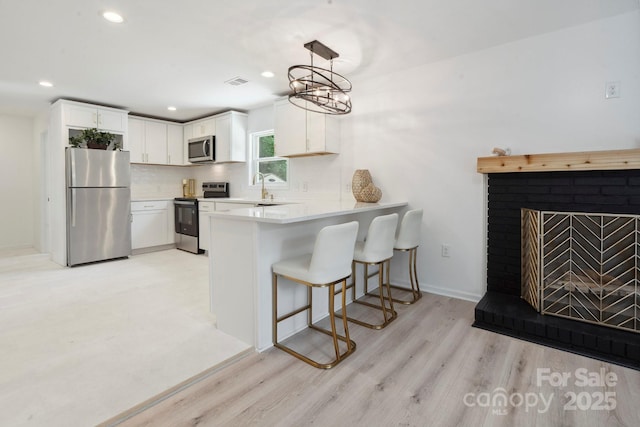 5420 Gwynne Ave, Charlotte, NC 28205 - kitchen with stainless steel appliances, a peninsula, light wood-style floors, a breakfast bar, and white cabinetry