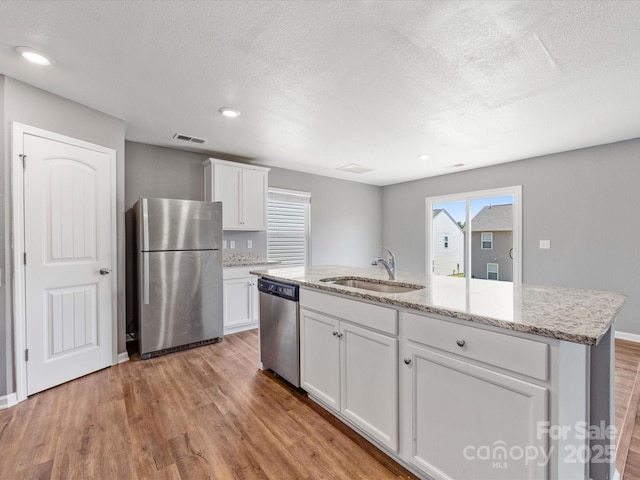 9136 Creedmore Hills Dr, Charlotte, NC 28214 - kitchen featuring appliances with stainless steel finishes, light wood finished floors, white cabinetry, a center island with sink, and light stone counters