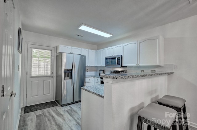 1504 Harpers Inlet Dr, Lake Wylie, SC 29710 - kitchen featuring stainless steel appliances, a peninsula, light wood-type flooring, white cabinetry, and a kitchen breakfast bar