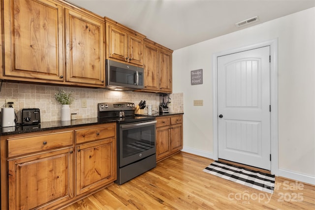 121 Maplewood Ct, Hudson, NC 28638 - kitchen featuring appliances with stainless steel finishes, brown cabinetry, tasteful backsplash, light wood-type flooring, and dark stone counters