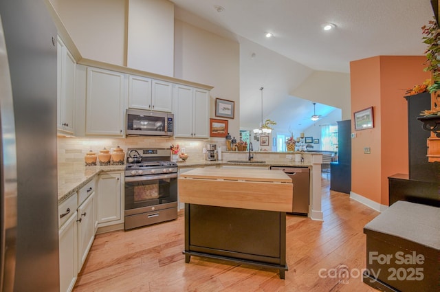 38 Westfield Way, Candler, NC 28715 - kitchen with stainless steel appliances, a peninsula, light wood finished floors, decorative backsplash, and high vaulted ceiling