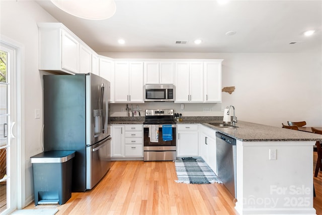 6507 Revolutionary Trl, Charlotte, NC 28217 - kitchen featuring appliances with stainless steel finishes, a peninsula, light wood-style floors, white cabinetry, and dark stone counters