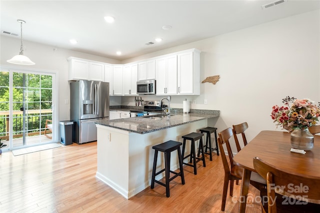 6507 Revolutionary Trl, Charlotte, NC 28217 - kitchen with stainless steel appliances, a peninsula, light wood-style floors, dark stone countertops, and white cabinetry
