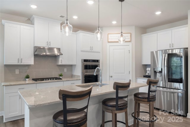 135 Orson Oaks Ln, Pineville, NC 28134 - kitchen featuring appliances with stainless steel finishes, under cabinet range hood, tasteful backsplash, a center island with sink, and white cabinets