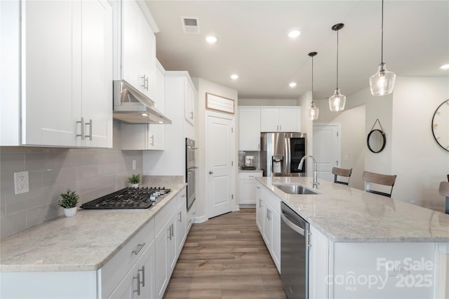 135 Orson Oaks Ln, Pineville, NC 28134 - kitchen featuring stainless steel appliances, under cabinet range hood, tasteful backsplash, light wood finished floors, and a kitchen island with sink