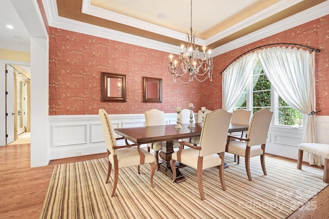 114 Thurstons Way, Mooresville, NC 28117 - dining room featuring light wood-type flooring, a chandelier, a raised ceiling, ornamental molding, and wainscoting