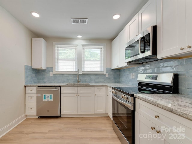 2414 Lane St, Kannapolis, NC 28083 - kitchen with appliances with stainless steel finishes, white cabinets, light wood-style flooring, light stone countertops, and backsplash