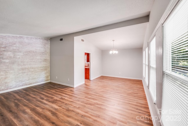 6513 Old Post Rd, Charlotte, NC 28212 - spare room featuring a chandelier, wood finished floors, lofted ceiling, brick wall, and an accent wall