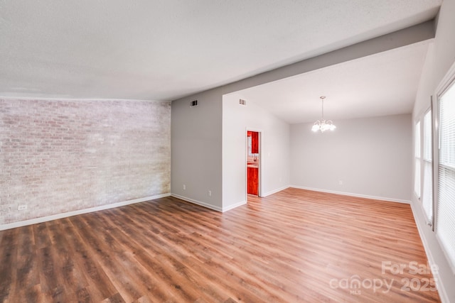 6513 Old Post Rd, Charlotte, NC 28212 - unfurnished room featuring brick wall, a chandelier, wood finished floors, and vaulted ceiling