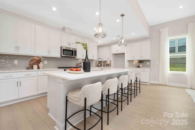1074 Wylie Falls Ln, York, SC 29745 - kitchen with stainless steel microwave, light wood-style floors, white cabinets, recessed lighting, and an island with sink