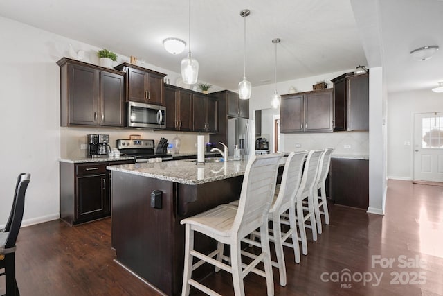 212 Fesperman Cir, Troutman, NC 28166 - kitchen featuring appliances with stainless steel finishes, dark wood finished floors, dark brown cabinets, a kitchen bar, and light stone counters