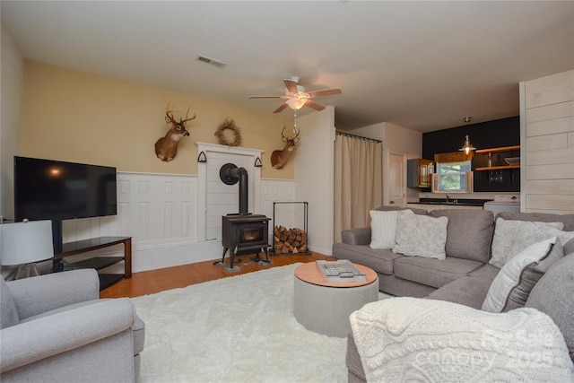 1239 Mac Ln, Stanley, NC 28164 - living room featuring wood finished floors, a wood stove, a ceiling fan, and wainscoting