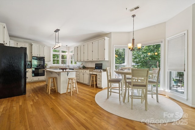4716 Heatherton Pl, Charlotte, NC 28270 - kitchen with black appliances, a chandelier, a kitchen breakfast bar, white cabinets, and light wood-style floors