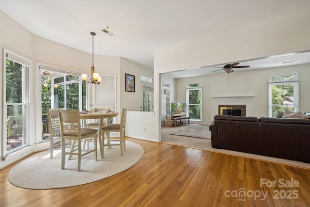 4716 Heatherton Pl, Charlotte, NC 28270 - dining area featuring wood finished floors, a chandelier, a ceiling fan, a brick fireplace, and healthy amount of natural light