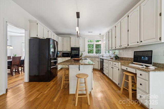 4716 Heatherton Pl, Charlotte, NC 28270 - kitchen with black appliances, light wood-style flooring, a kitchen bar, tasteful backsplash, and a center island