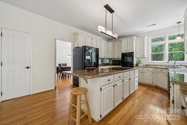 4716 Heatherton Pl, Charlotte, NC 28270 - kitchen with light wood-type flooring, a center island, white cabinets, a kitchen breakfast bar, and black appliances