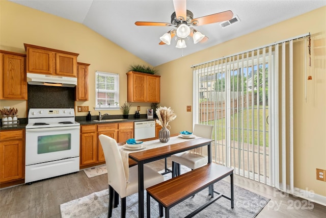7616 Shiny Meadow Ln, Charlotte, NC 28215 - kitchen with white appliances, under cabinet range hood, lofted ceiling, dark countertops, and brown cabinetry
