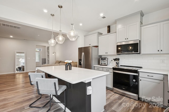 13323 Savaine St, Charlotte, NC 28278 - kitchen featuring appliances with stainless steel finishes, wood finished floors, decorative backsplash, a kitchen island, and light countertops